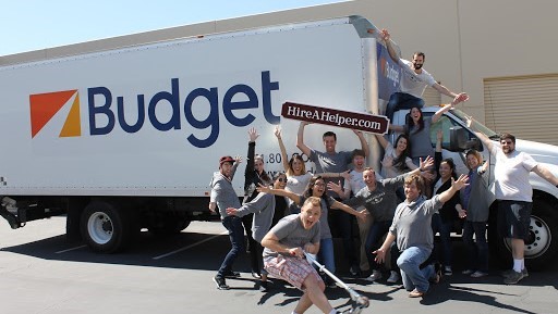 Employees with hands in the air holding HireAHelper sign in front of Budget Truck