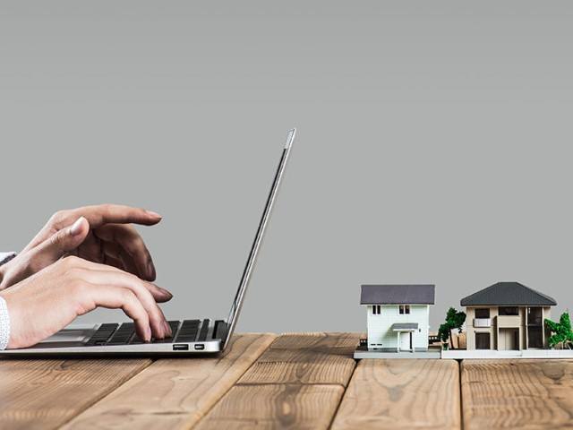 Hands typing on a laptop with miniature houses next to it.