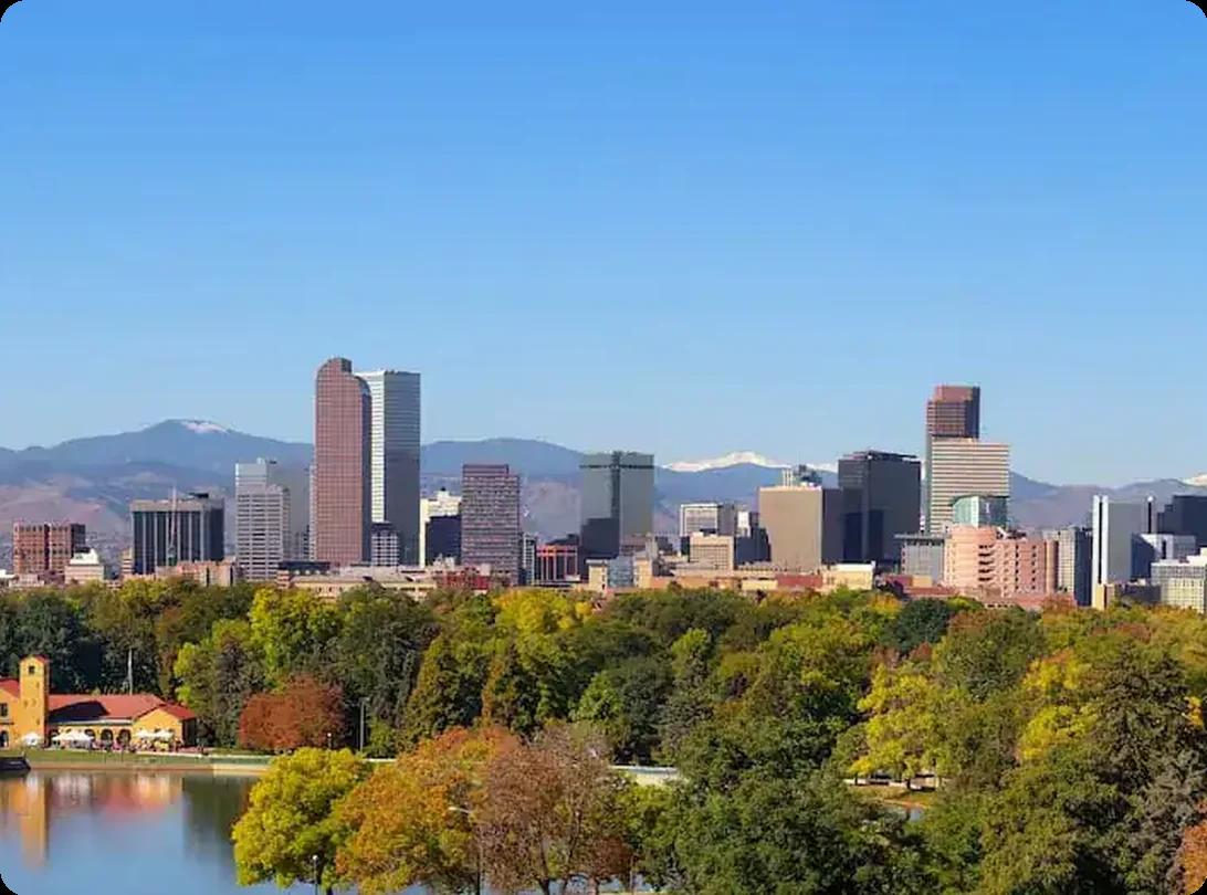 Denver skyline viewed from City Park with fall foliage and mountains in the background.