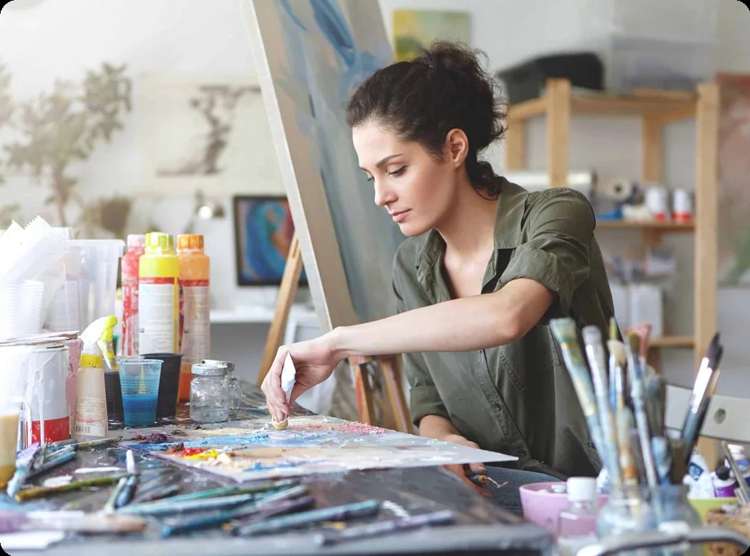 An artist carefully packing brushes, paints, canvases, and art tools into protective boxes for a move