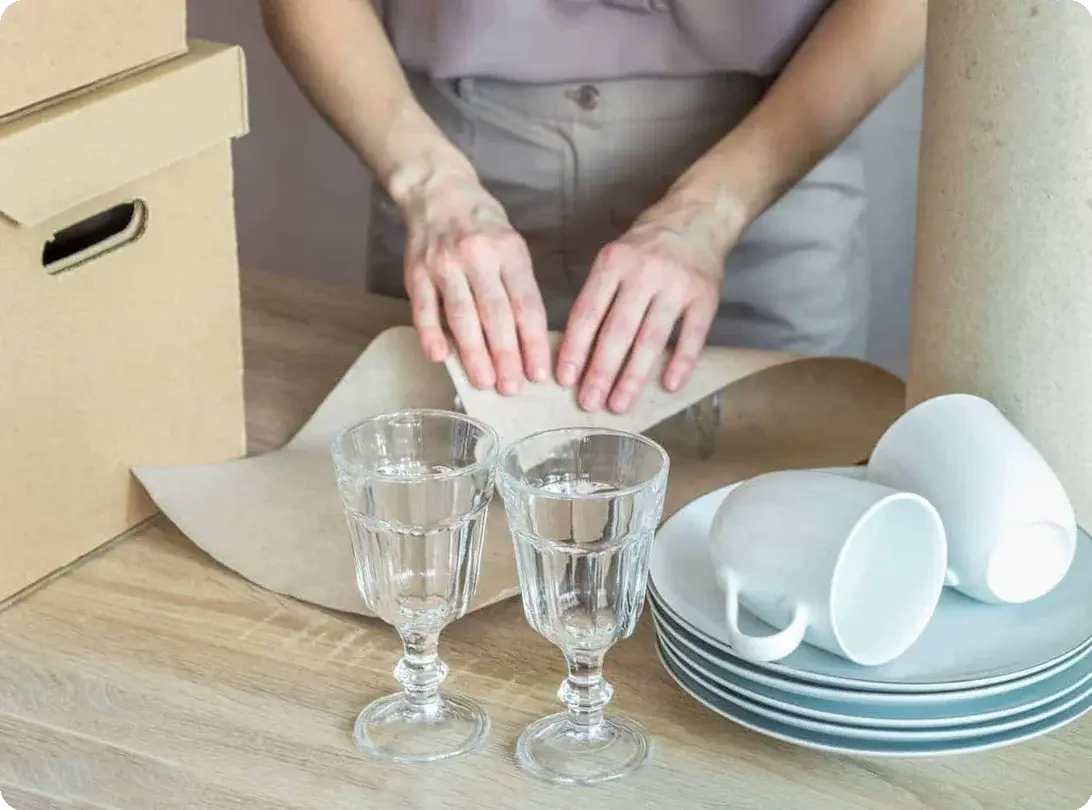 a person wrapping and packing away dishes, glassware, and mugs