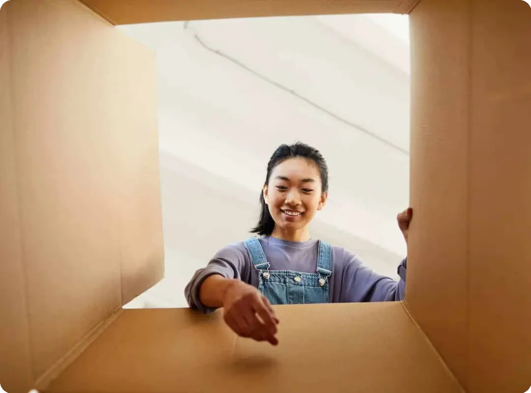 A woman sets down an item into a box. The angle of the shot is from the bottom of the box pointing upwards, so it looks as through the woman is reaching towards the camera