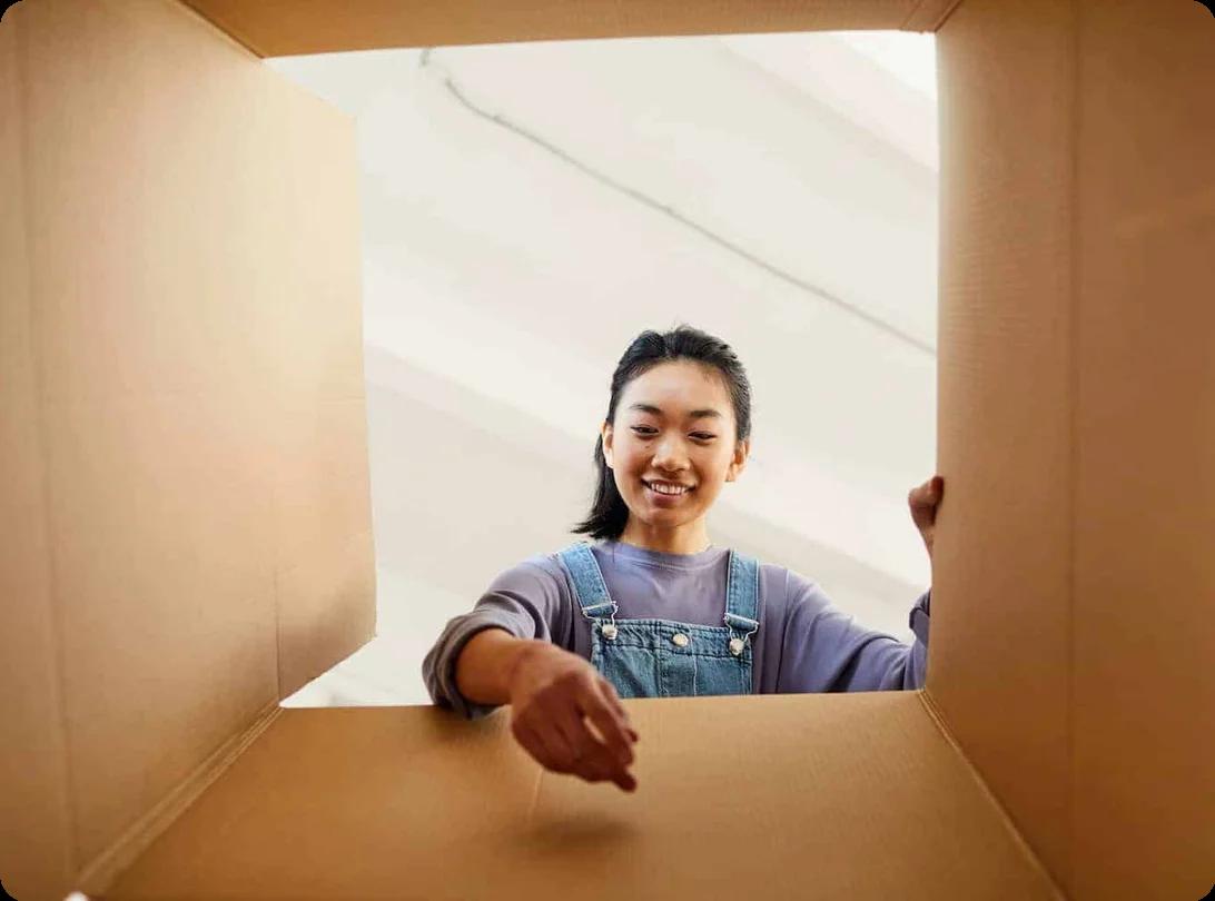 A woman sets down an item into a box. The angle of the shot is from the bottom of the box pointing upwards, so it looks as through the woman is reaching towards the camera