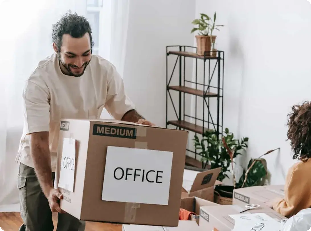 A woman is packing a box, and a man is carrying another one labeled "office" suggesting they are moving out
