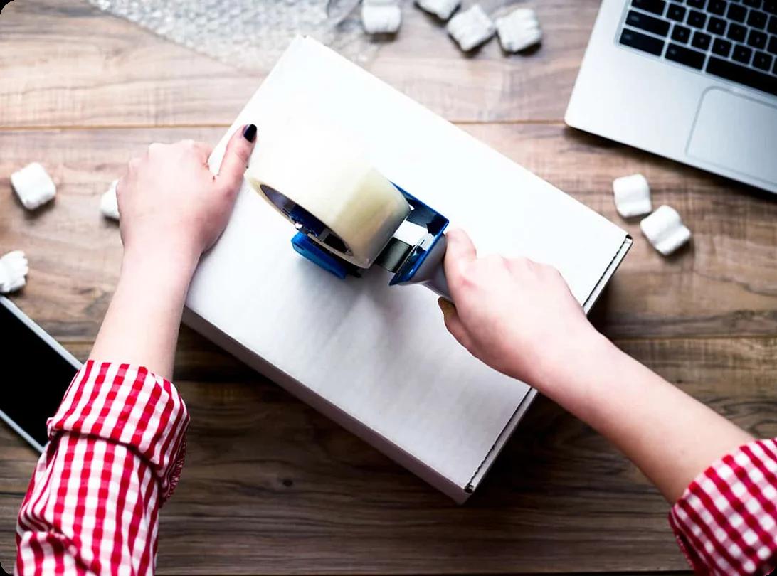 A woman holding multiple rolls of clear packing tape and a tape dispenser