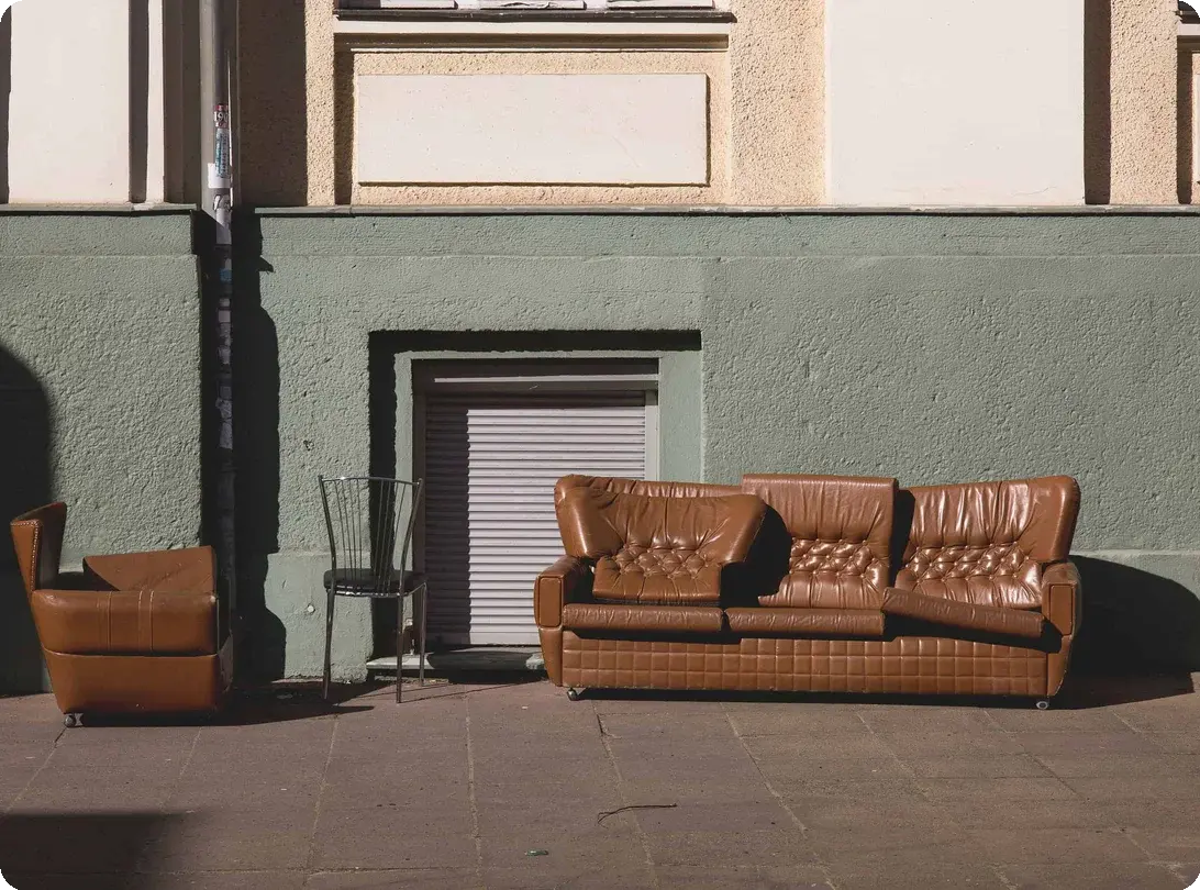 A leather sofa and matching armchair left on a city sidewalk awaiting donation pickup