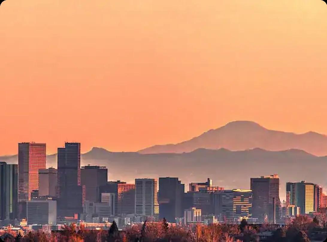 Denver CO cityscape with mountain backdrop during sunset