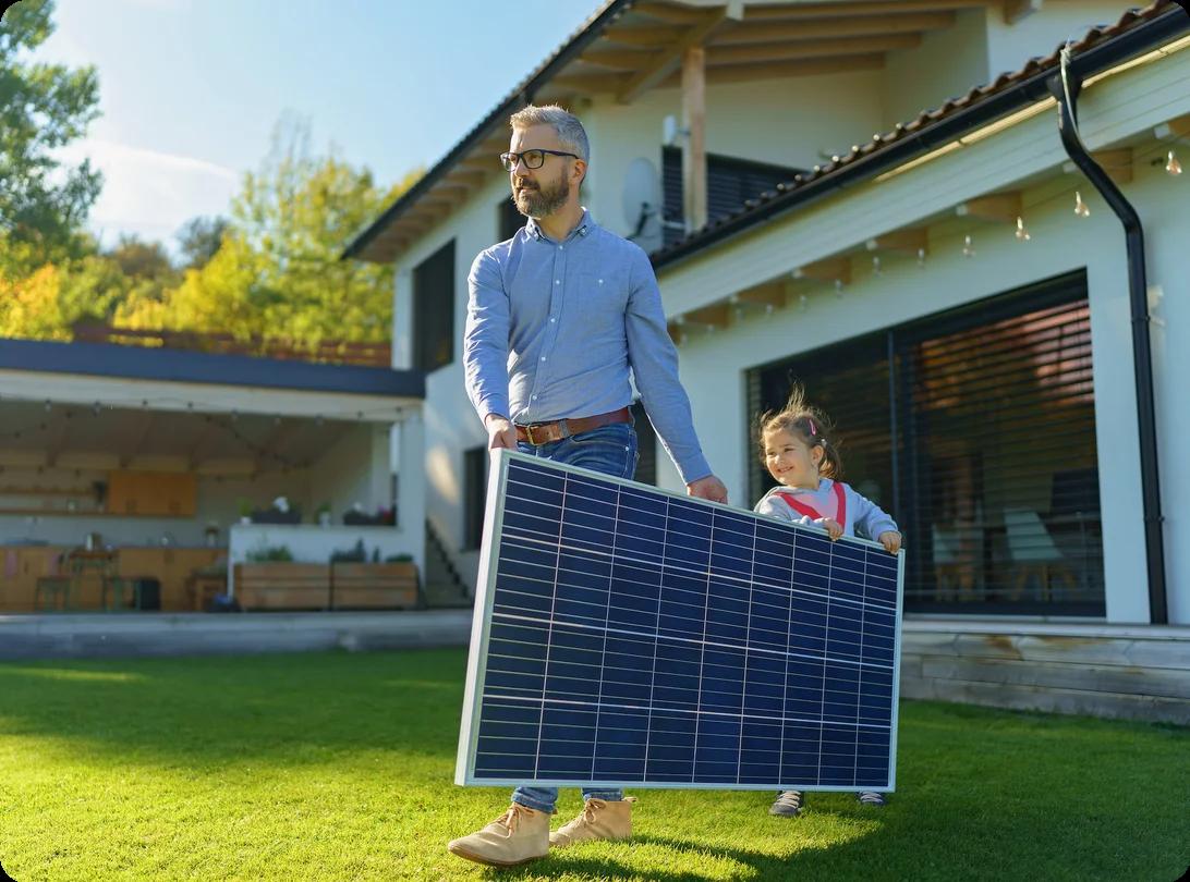 a father and daughter move a solar panel by carrying it across a lawn