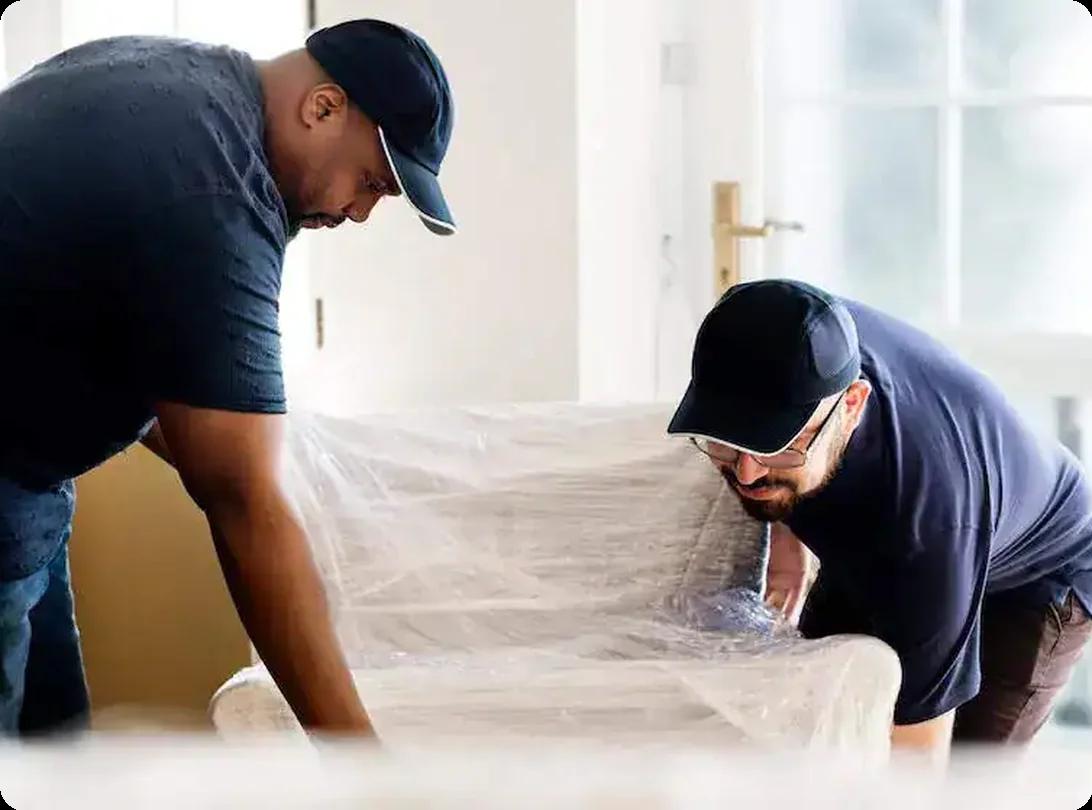 Professional movers carrying wrapped furniture inside a home during a relocation
