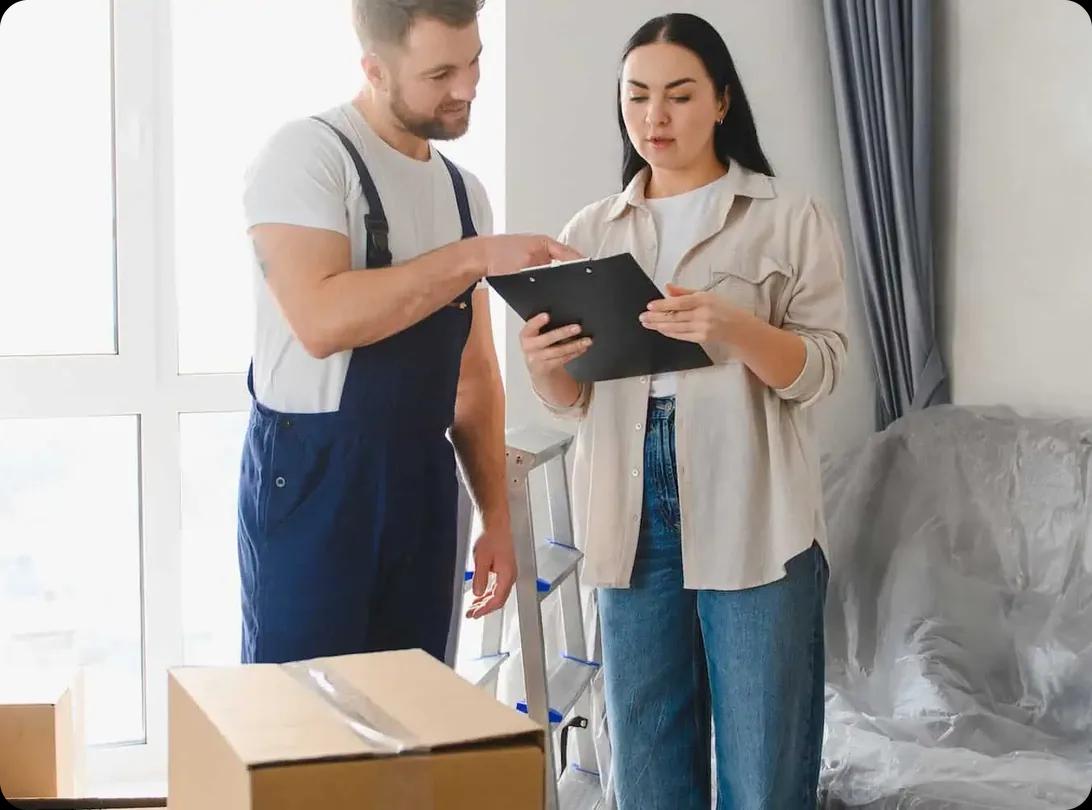 A mover reviewing paperwork on a clipboard with a customer in a partly packed room