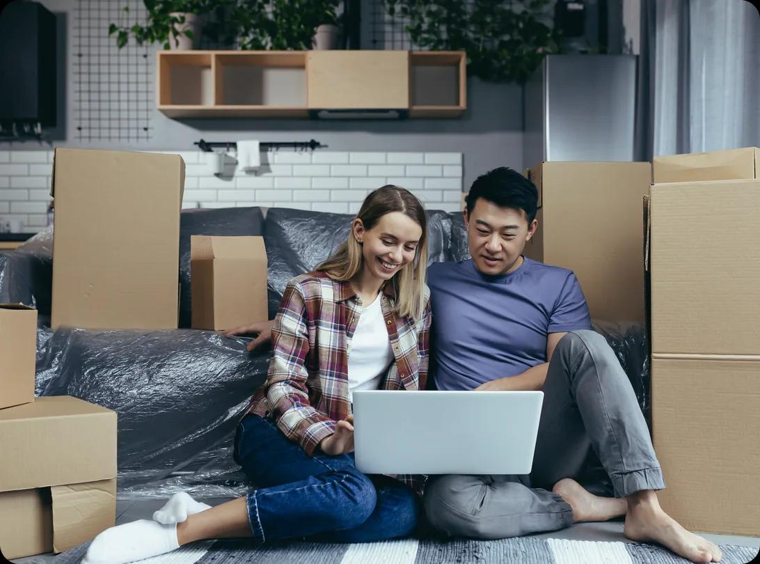 A couple sitting on the floor among boxes looking at a laptop
