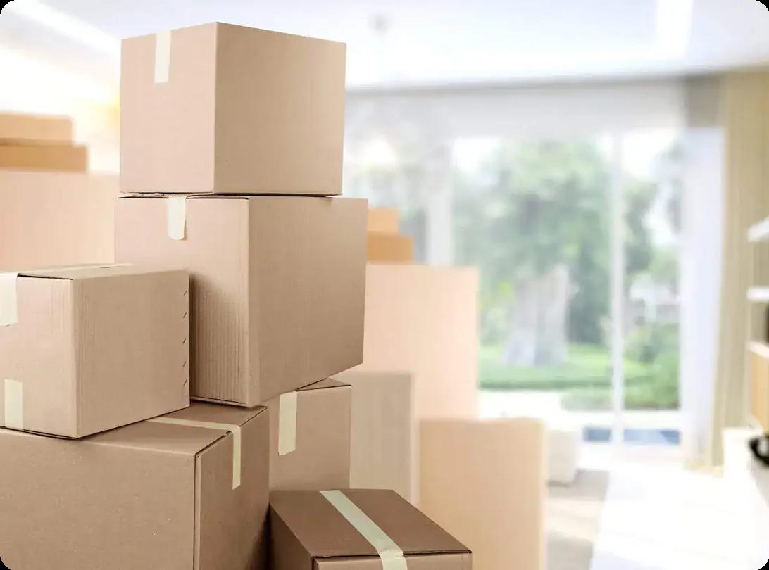 Stacked cardboard moving boxes in a bright living room, ready for a home relocation.