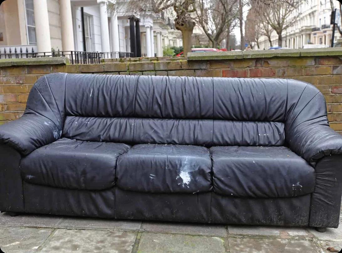 an old black couch is sitting at the curb