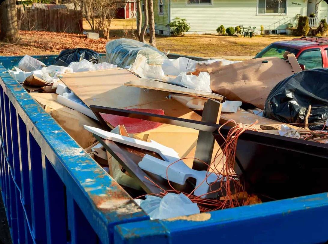 A dumpster full of broken furniture and various other kinds of junk