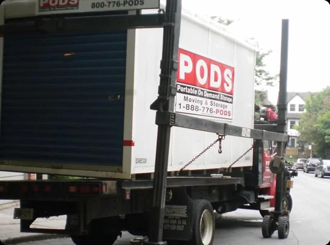 A homeowner carefully loading boxes and furniture into an open PODS moving container parked in the driveway