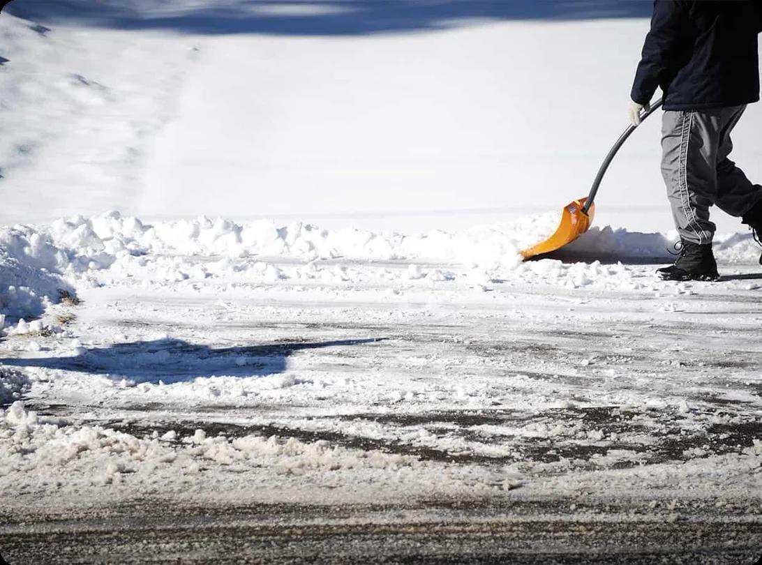 A person spreading rock salt onto an icy driveway after a winter storm