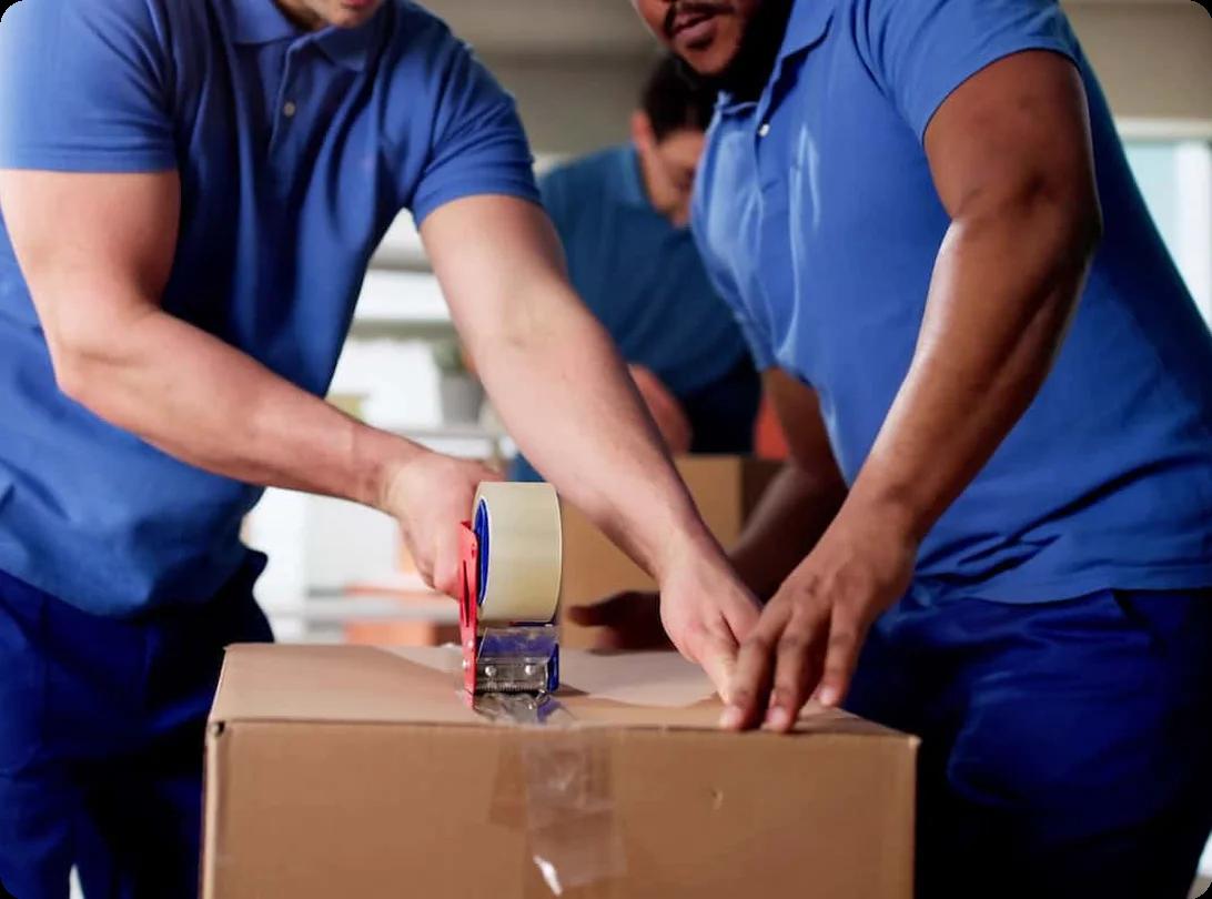 a team of movers in blue uniforms tapes a box shut