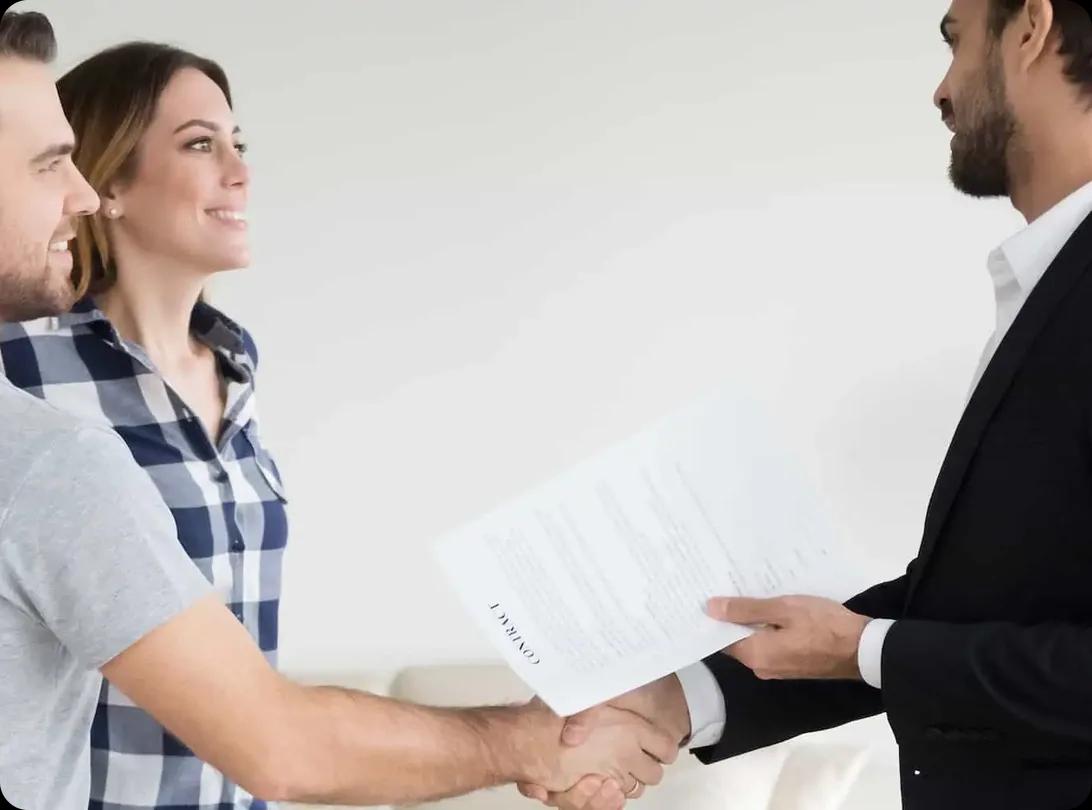 A couple shaking hands with a property manager who is holding a lease contract.