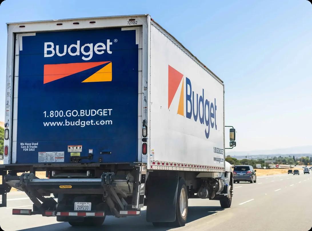 Budget moving truck traveling on open road under clear sky