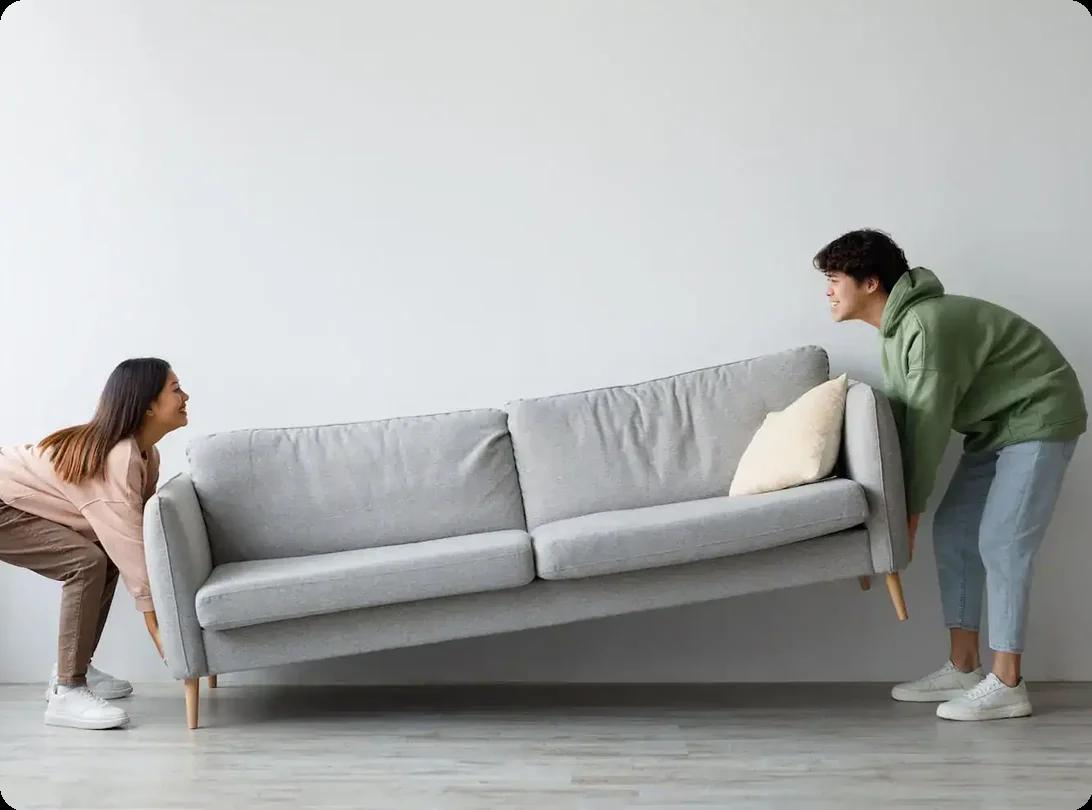 two people work together to lift a gray couch