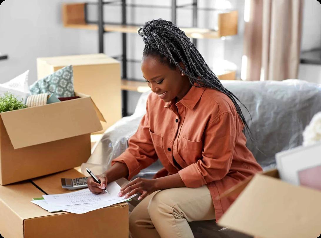 a woman calculates the cost of a move with a calculator, surrounded by packed boxes