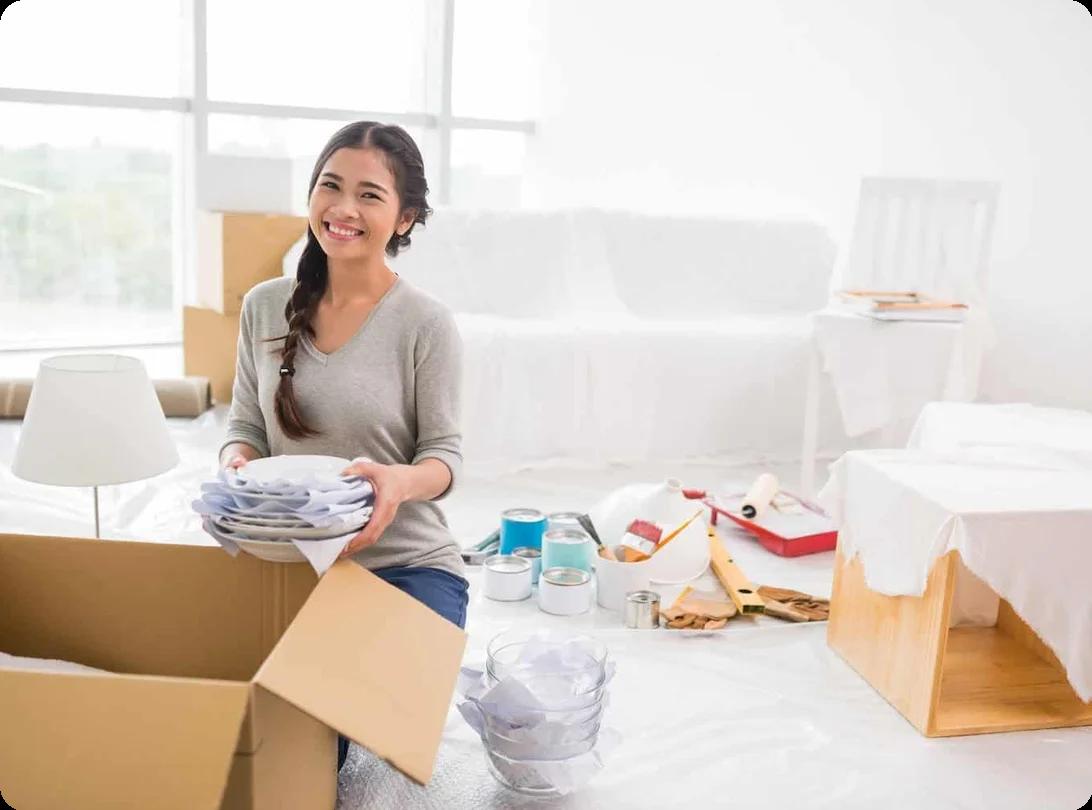 a young woman smiles as she packs dishes into a box