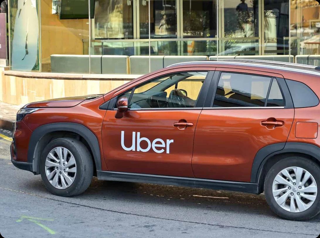 A copper colored compact suv with UBER written on the side drives down the road