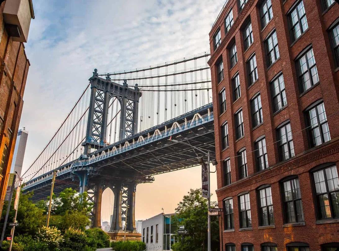 a view of the brooklyn bridge from between two brick buildings