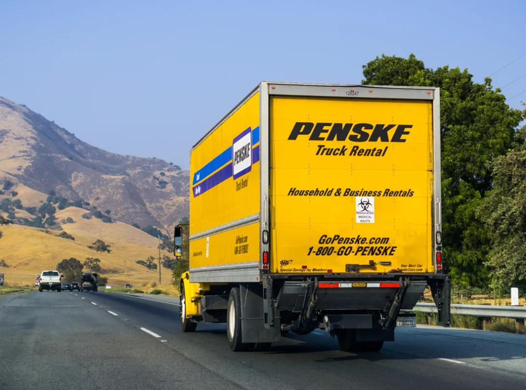 an image of a penske rental truck driving on a highway with snow-capped mountains in the background