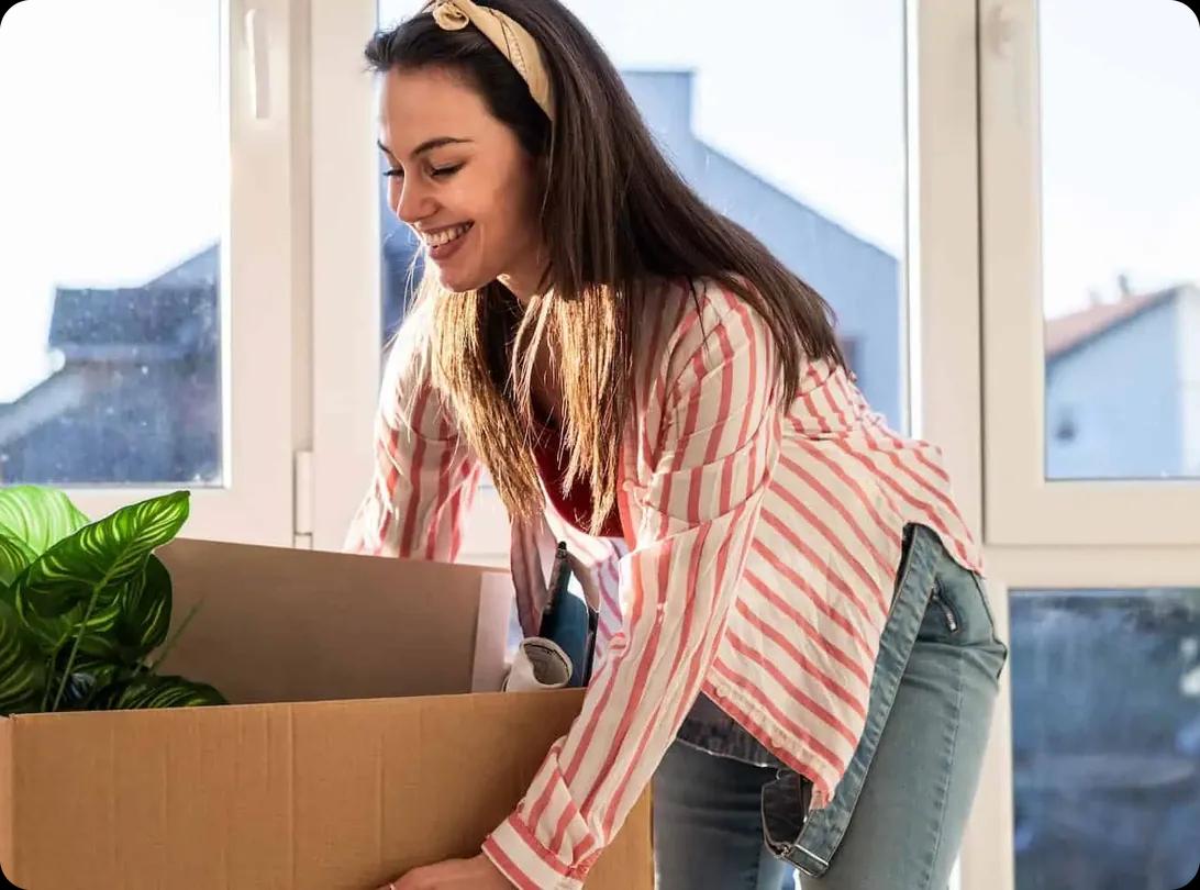 A woman lifting a packed box in a bright studio apartment