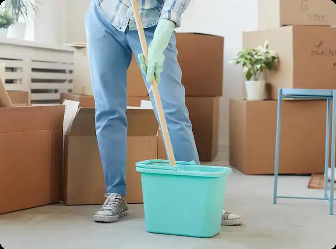 Person mopping the floor in a room filled with moving boxes during a move-out cleaning