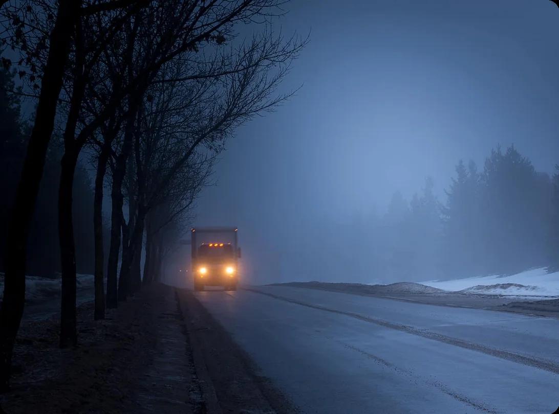 A rental moving truck driving carefully on a snow-covered highway with winter conditions and reduced visibility