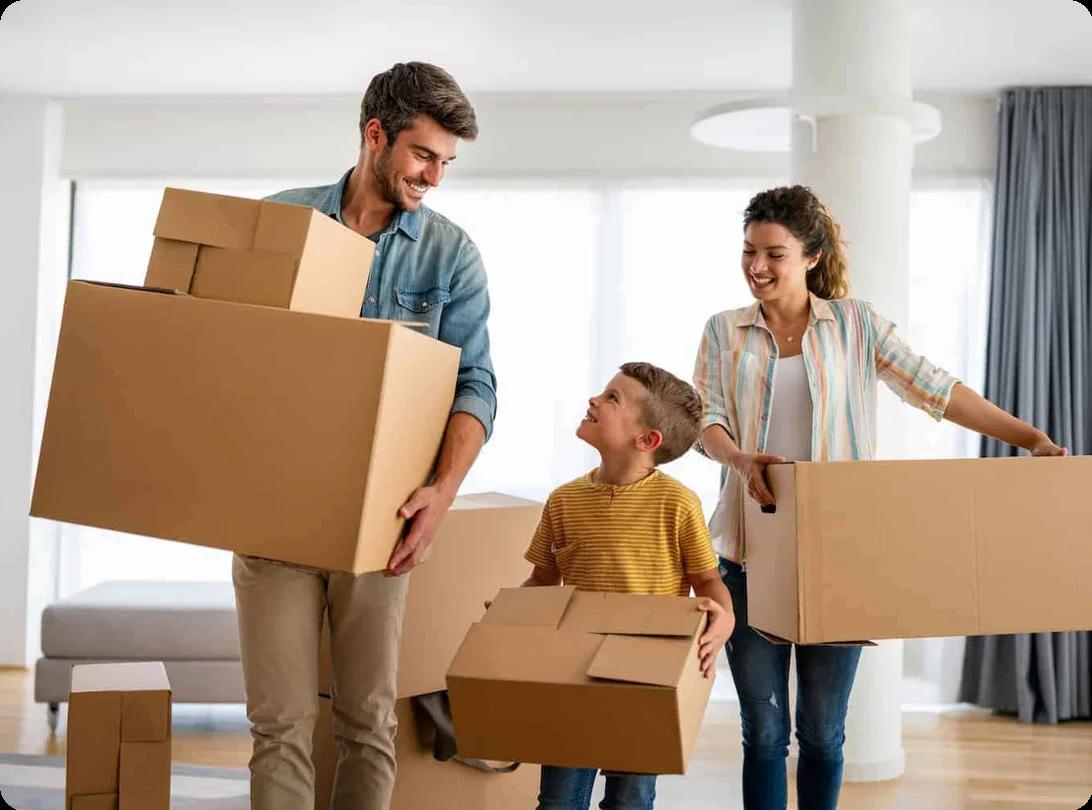 A father, mother, and young son all happily carry packed moving boxes