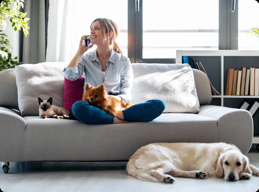 A woman sits on her couch in her apartment with her cat and two dogs