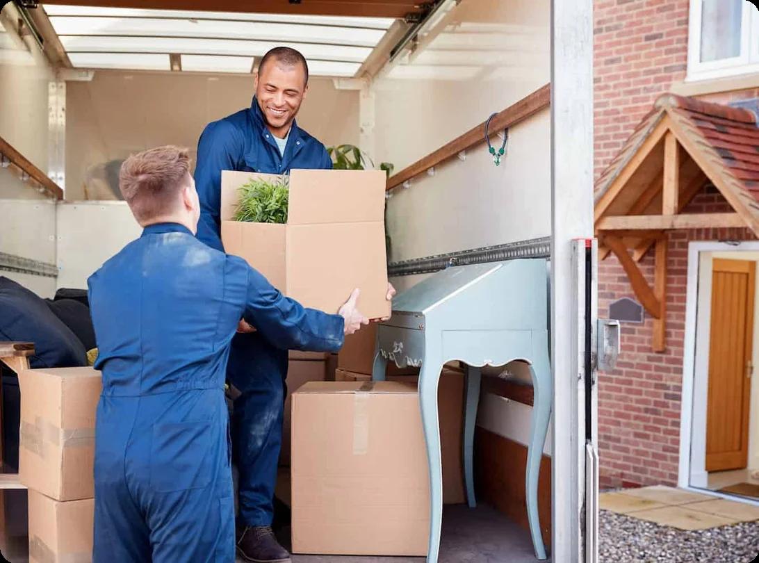 two movers in blue coveralls unload boxes from a truck