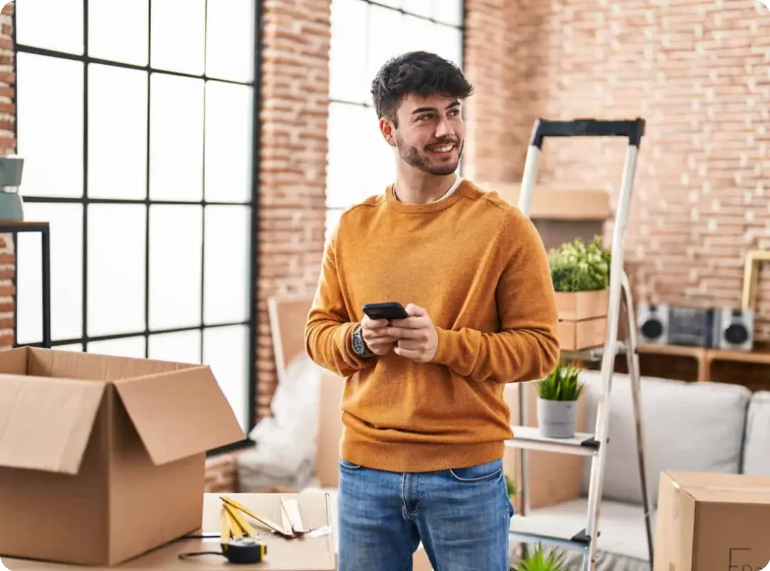 a man stands in a room full of moving boxes while holding his smart phone