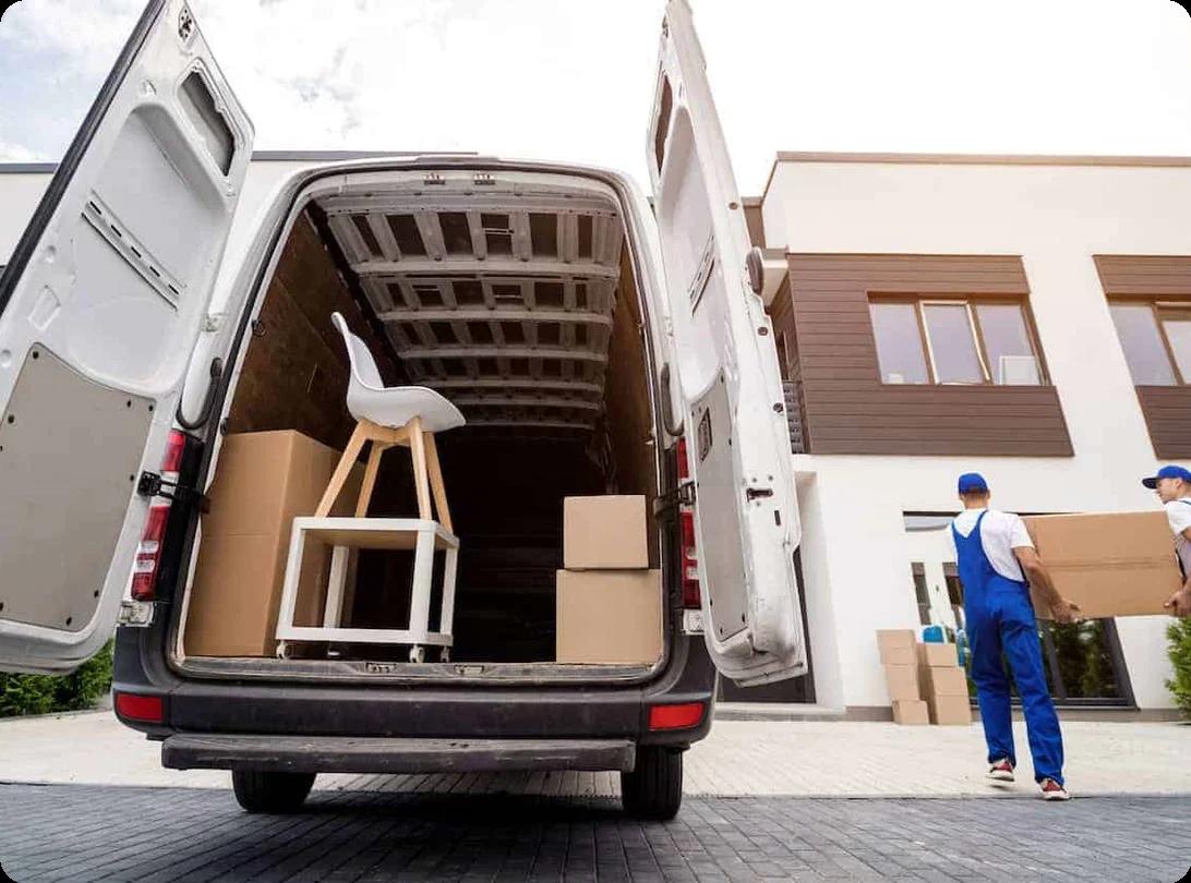 movers carry a box into a home. There are more items in the back of an open moving truck