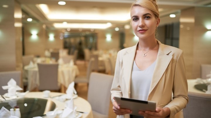 Event Planner holding a tablet computer standing in front of fancy dinner tables
