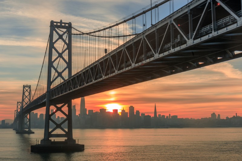 A view of the San Francisco Bay Bridge at sunset with San Francisco, CA, city line in the background.