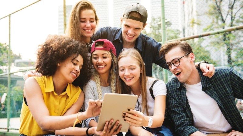 People outside smiling and looking at a tablet computer