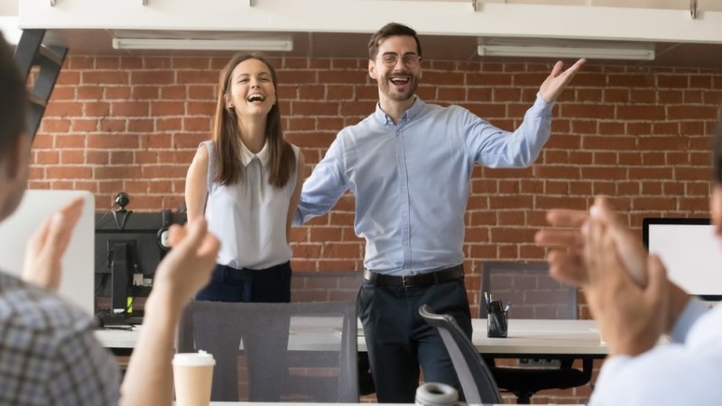Two people standing and smiling in front of other people clapping
