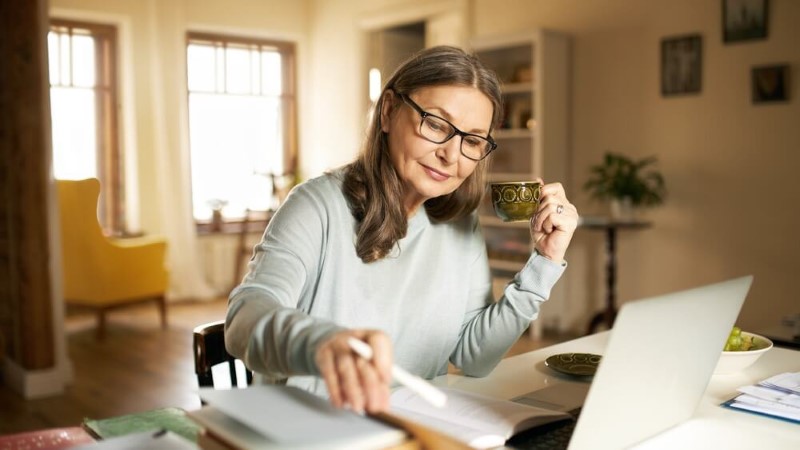 Retiree sitting at a desk reading a book and drinking tea