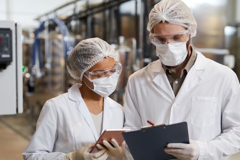 Two people wearing safety gear consult with each other in a lab